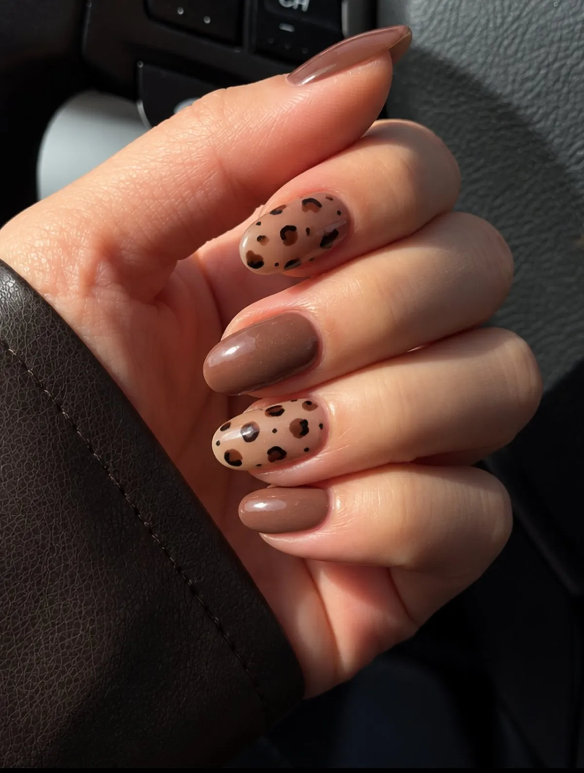 Short rounded nails in glossy cocoa brown, with two sheer nude accent nails painted with dark leopard spots.