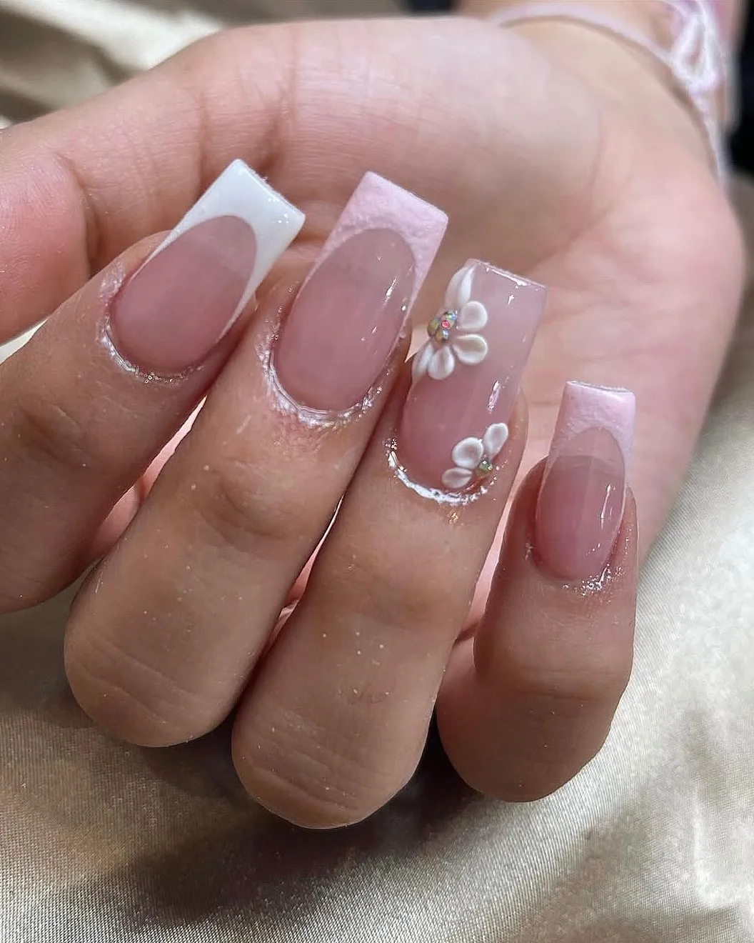 Square nails with a soft pink French tip and white 3D flowers on one nail.