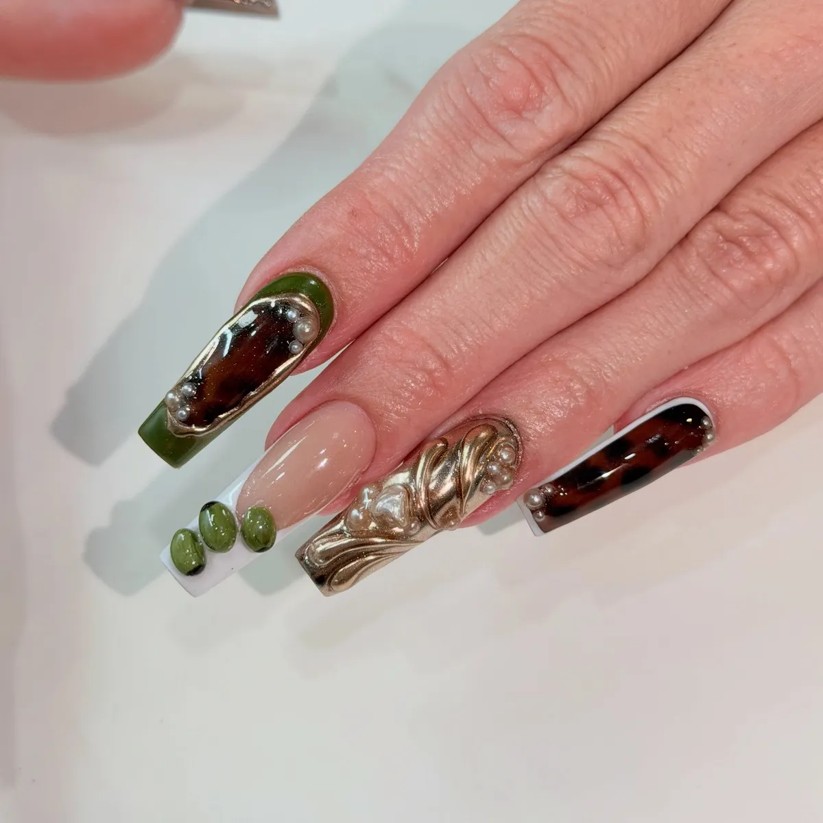 Coffin nails with olive-green frames, tortoiseshell centres, gold chrome swirls and pearls.