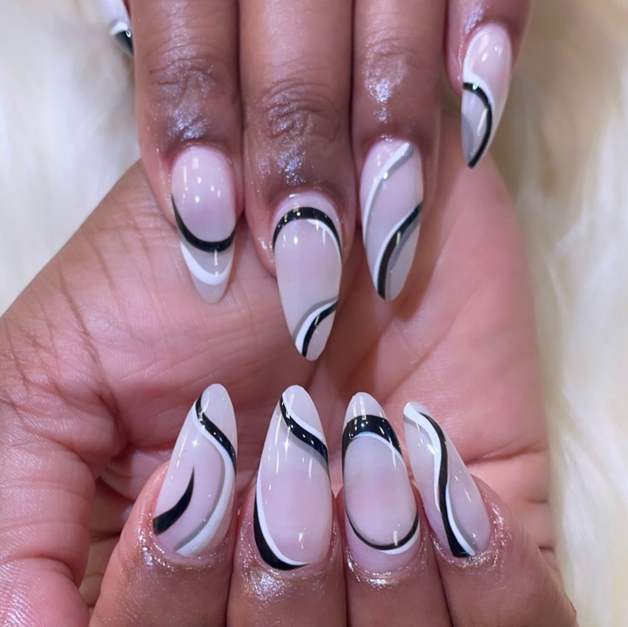 Almond nails with a milky-pink base decorated with abstract black, white, and grey wavy line art.