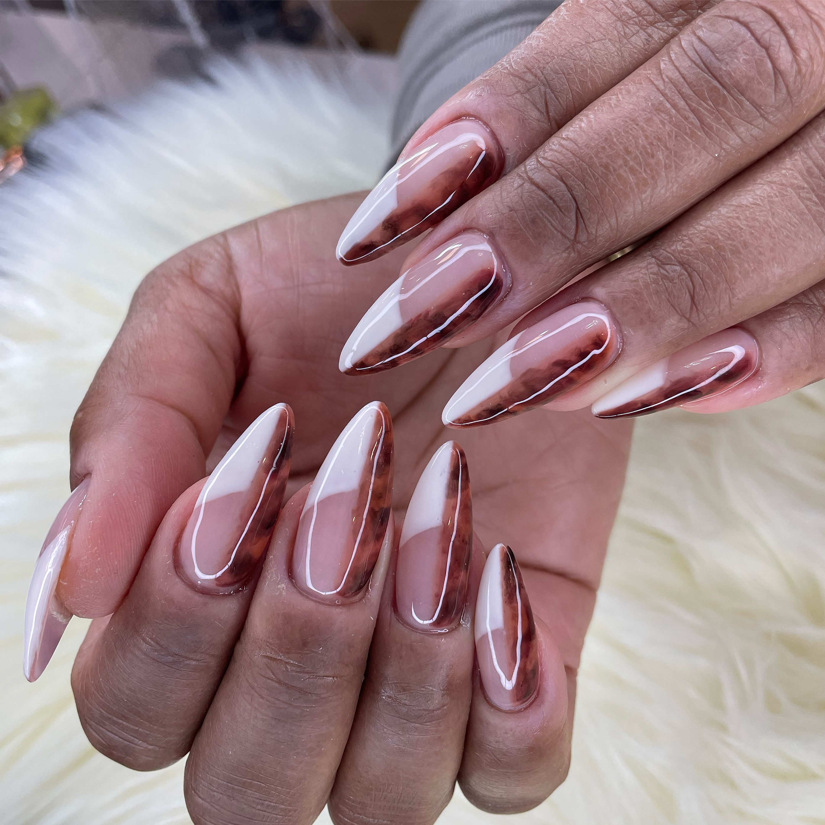 Long almond nails with a diagonal split design of nude base and brown tortoiseshell pattern under a high-gloss finish.