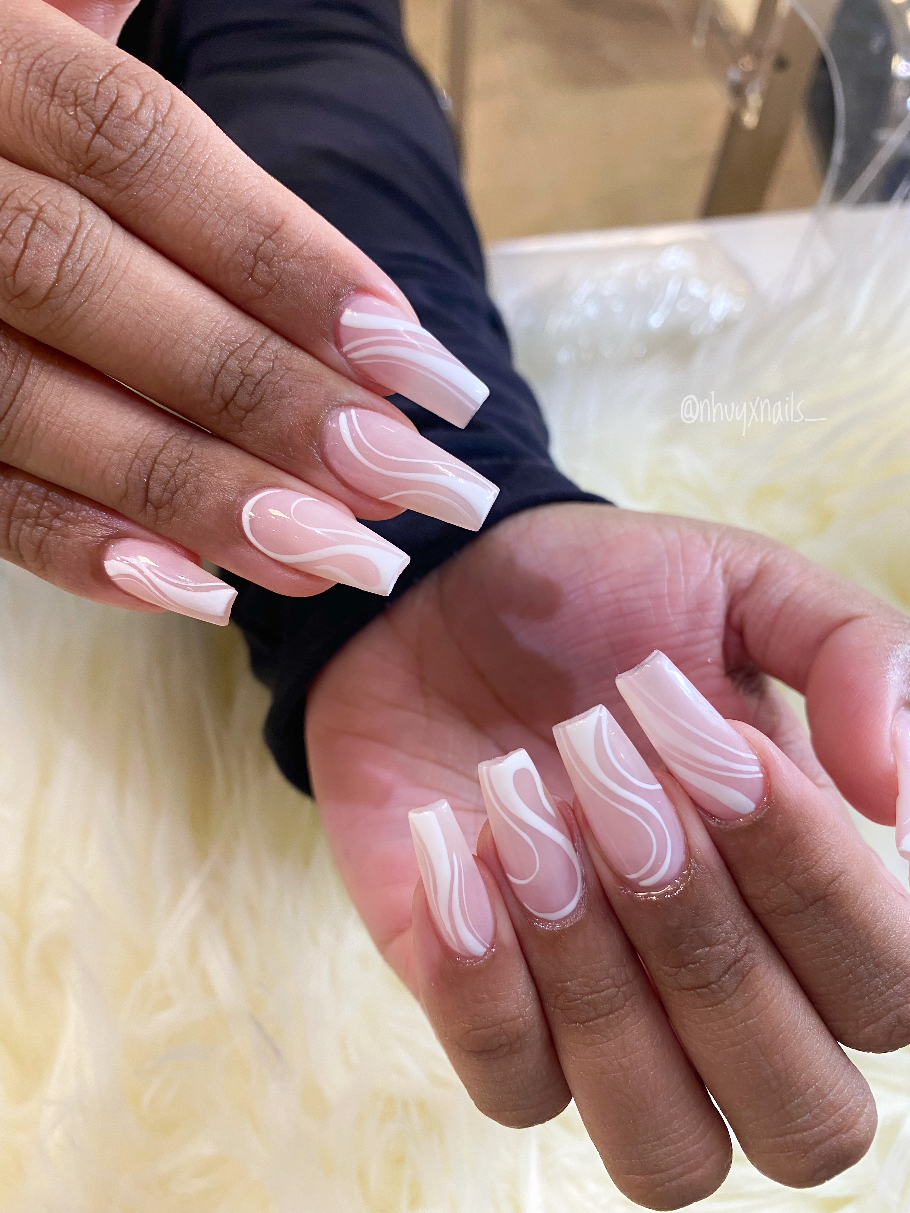 Long coffin nails with a translucent nude-pink base and fine white wavy swirl line art on white faux fur.