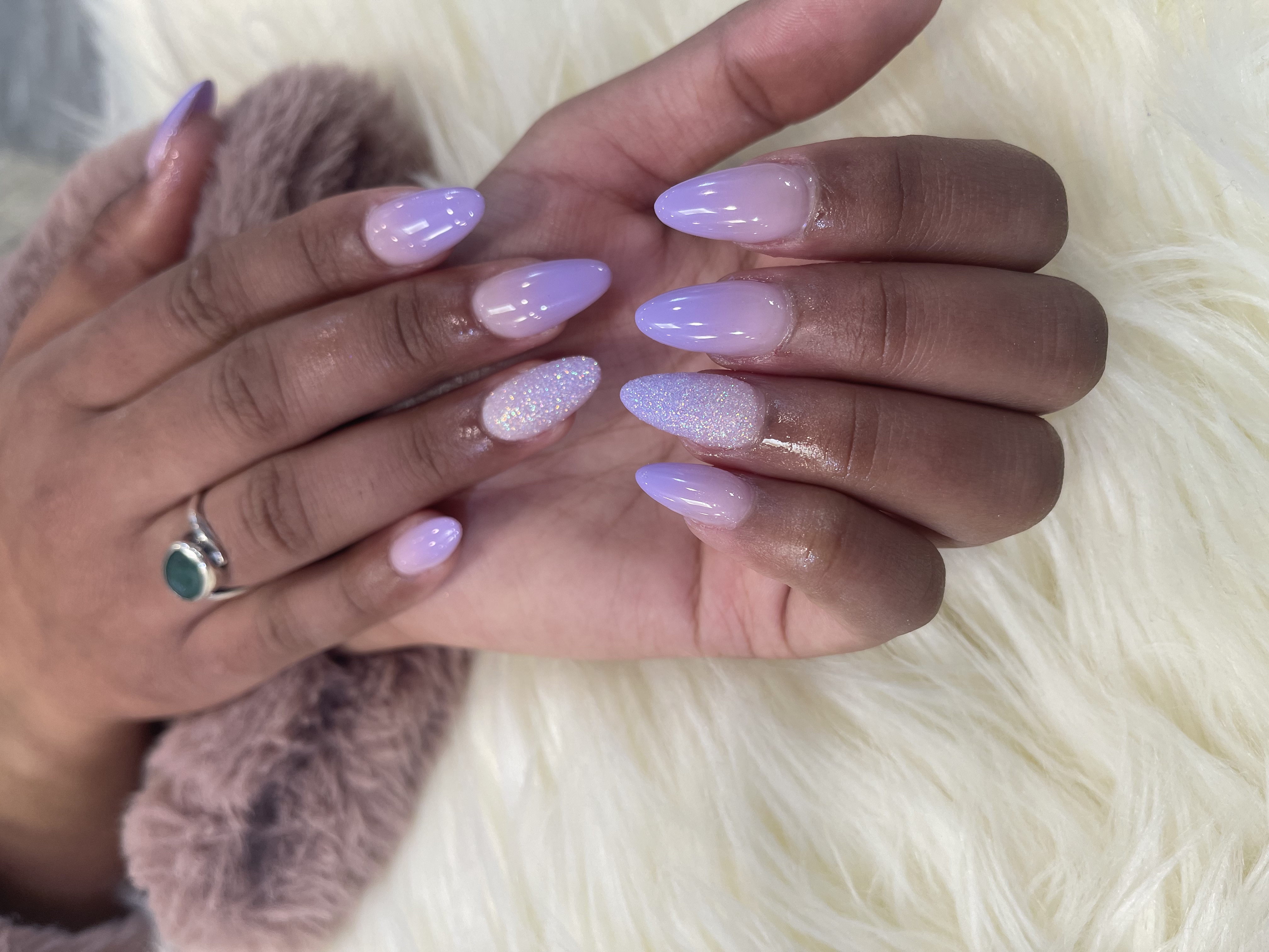 Almond nails with a light purple-to-white ombre gradient and iridescent white glitter accent nails on white faux fur.