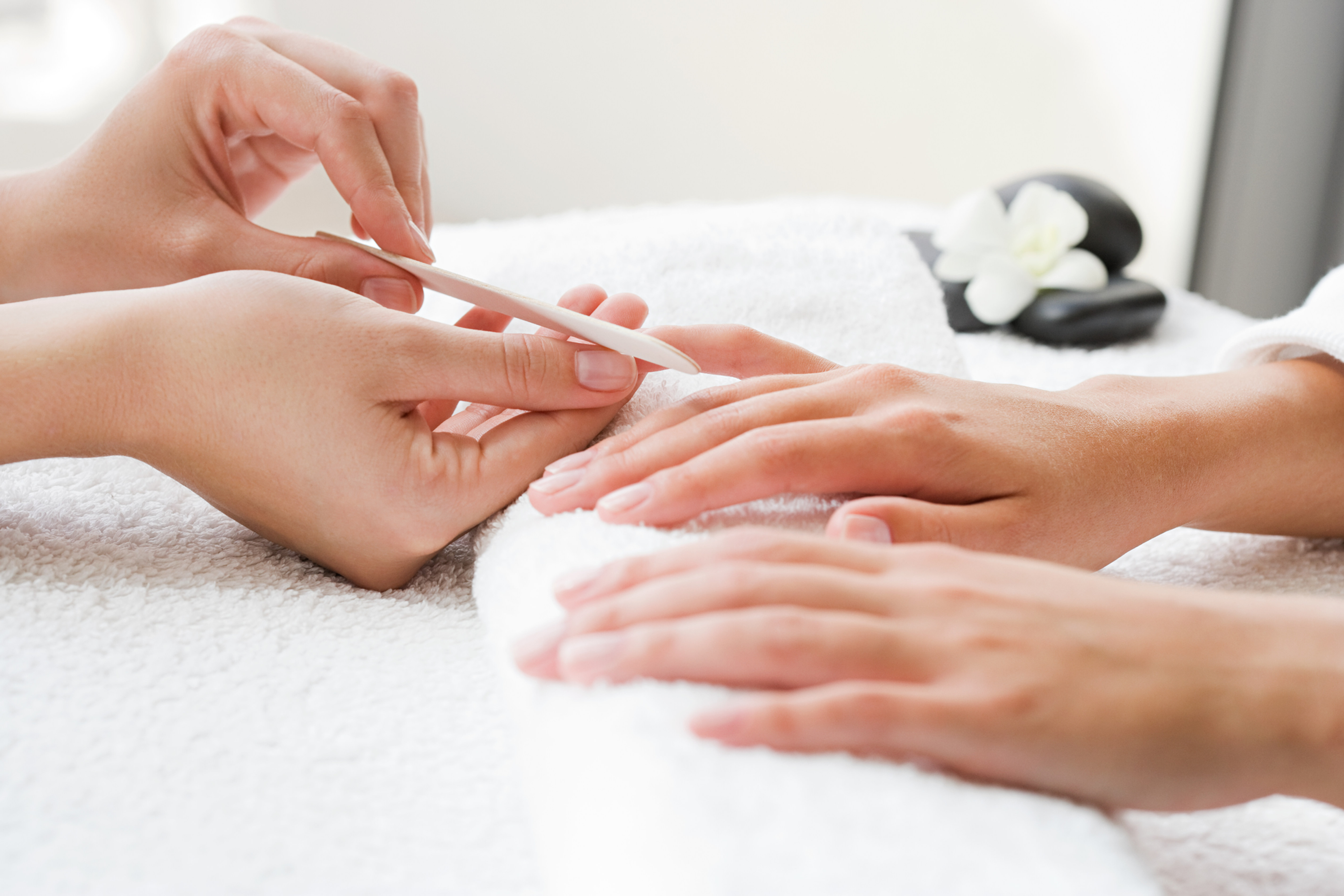 Manicurist filing a client's fingernails over a white towel in a bright spa setting with black stones and a white orchid.
