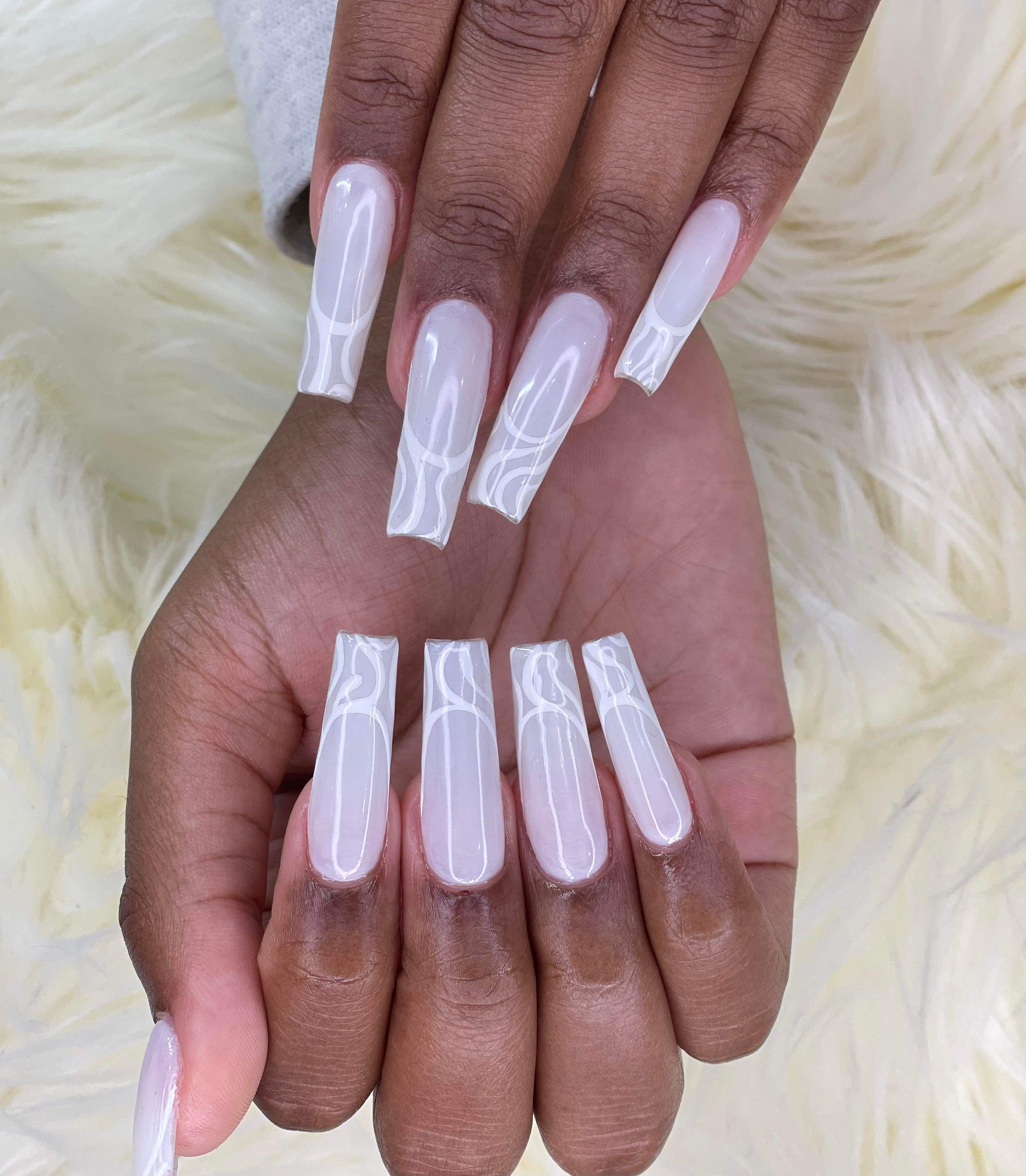 Long square nails with a translucent milky-white base and abstract white swirl patterns on the tips against white faux fur.