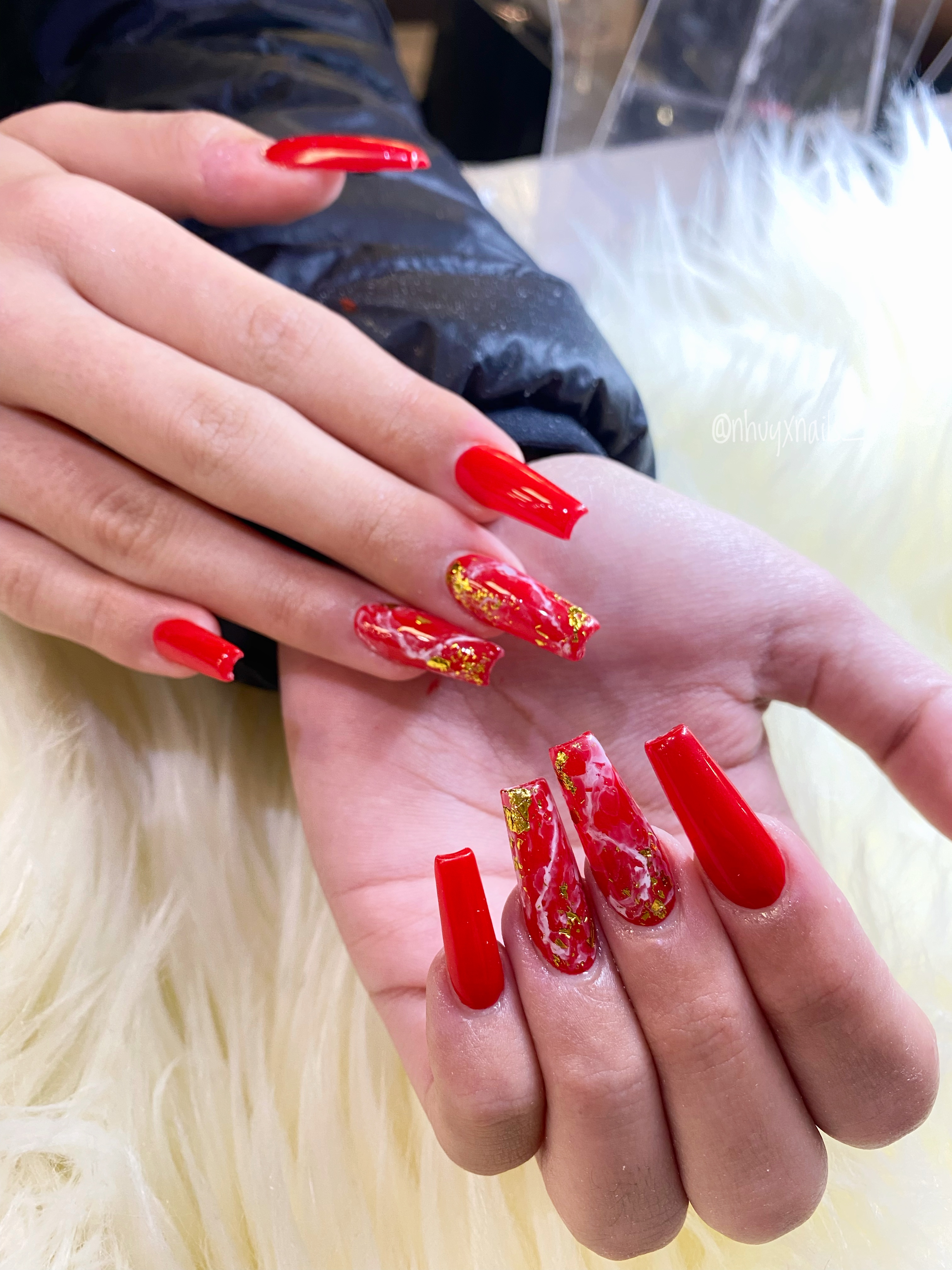 Long coffin nails in glossy red with red-and-white marble accent nails and gold foil flakes on white faux fur.